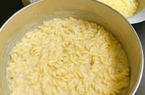 Creamy pasta being stirred in a pan with garlic, olive oil, and sun-dried tomatoes — a rich, home-cooked meal in the making.
